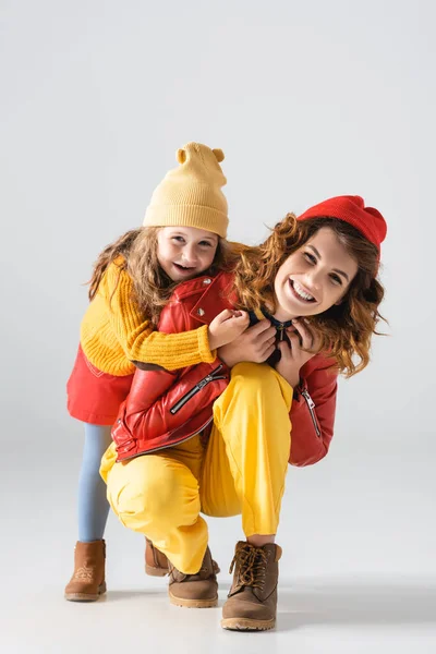 Madre e hija en trajes coloridos rojos y amarillos abrazándose sobre fondo gris - foto de stock