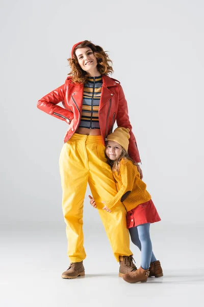 Daughter in colorful red and yellow outfit hugging mother leg on grey background — Stock Photo