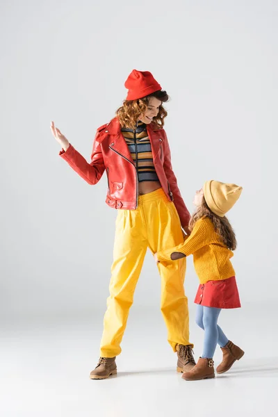 Daughter in colorful red and yellow outfit hugging mother leg on grey background — Stock Photo