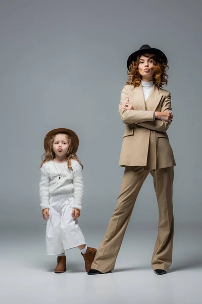 Elegant mother and daughter in white and beige outfits showing kiss on grey — Stock Photo