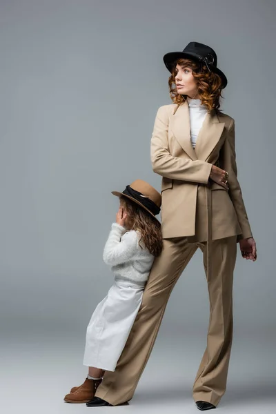 Elegante madre e hija en trajes blancos y beige posando sobre gris - foto de stock