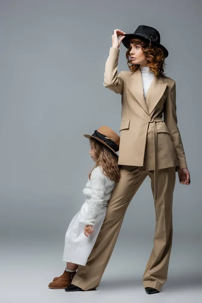 Elegante madre e hija en trajes blancos y beige posando sobre gris - foto de stock