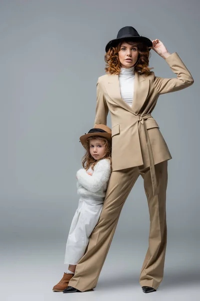 Elegante madre e hija en trajes blancos y beige posando sobre gris - foto de stock