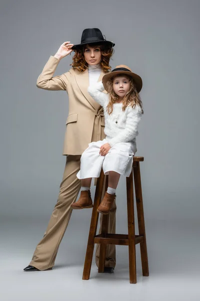 Elegant mother and daughter in white and beige outfits posing on chair on grey — Stock Photo