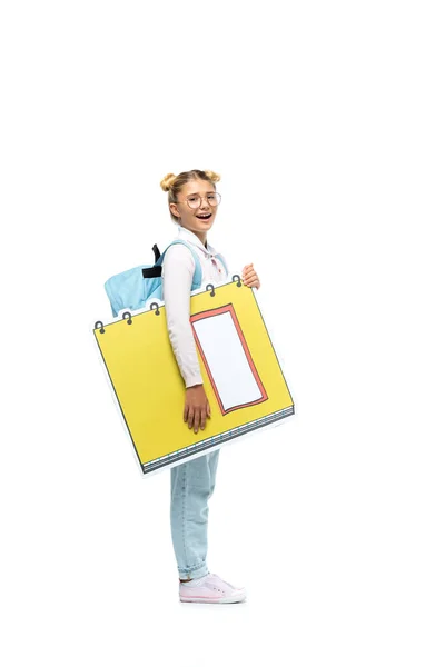 Full length view of excited schoolgirl in eyeglasses holding paper cut copy book while looking at camera on white — Stock Photo