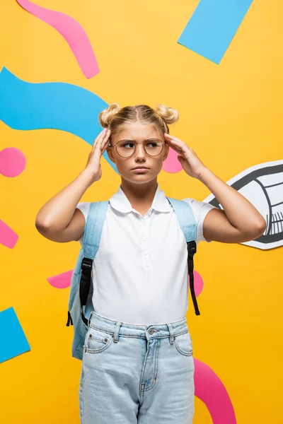 Tired schoolchild in eyeglasses touching head near paper pencil and colorful elements on yellow — Stock Photo