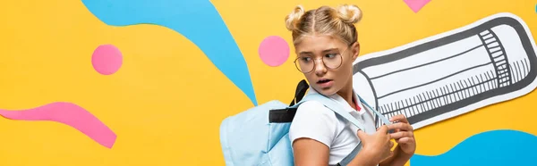 Horizontal image of surprised schoolkid looking at backpack near paper pencil and decorative elements on yellow — Stock Photo