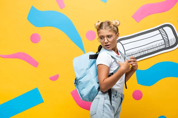 Shocked pupil looking at backpack on yellow background with paper pencil and abstract elements — Stock Photo