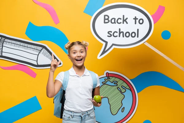 Écolière avec pomme ayant idée près de retour à l'école lettrage sur bulle de la parole et l'art du papier sur fond jaune — Photo de stock