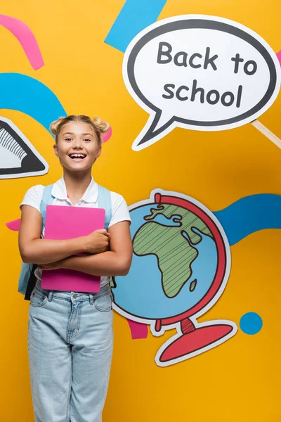 Schoolchild holding laptop beside speech bubble with back to school lettering and paper elements on yellow background — Stock Photo