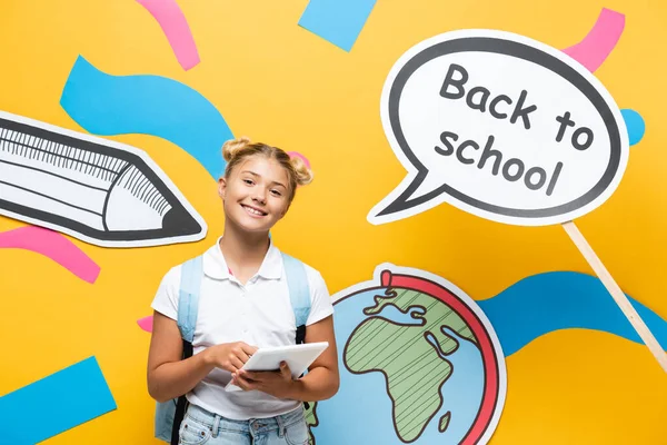 Schoolchild holding digital tablet near paper speech bubble with back to school lettering on yellow background — Stock Photo