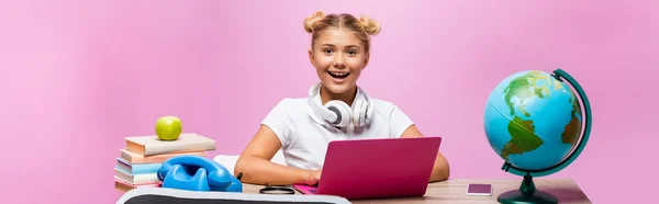 Cosecha horizontal de niño en auriculares sentados cerca de gadgets, globo y libros sobre fondo rosa - foto de stock