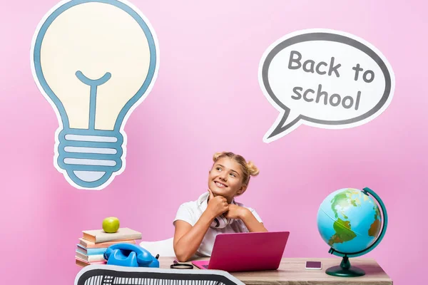 Schoolkid sitting near globe, gadgets and paper artwork on pink background — Stock Photo