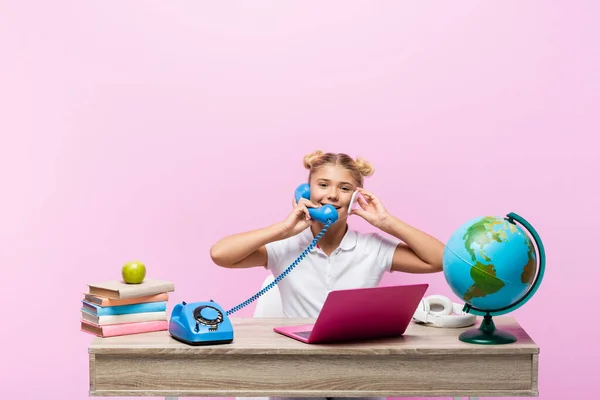 Schoolkid talking on smartphone and telephone near books and globe isolated on pink — Stock Photo