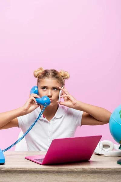 Schoolkid talking on telephone and smartphone near globe and laptop on table isolated on pink — Stock Photo