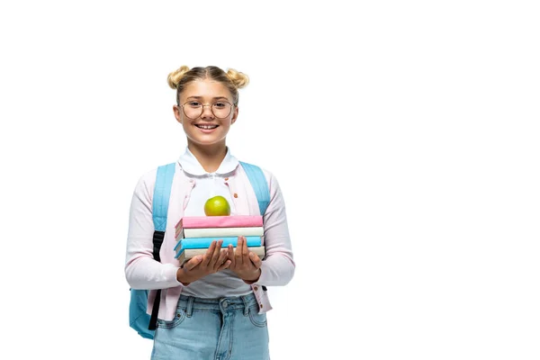 Schulkind mit Rucksack hält Apfel und Bücher in der Hand, während es isoliert auf weiß in die Kamera blickt — Stockfoto