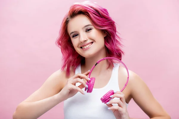 Jeune femme aux cheveux colorés tenant des écouteurs isolés sur rose — Photo de stock