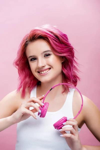 Giovane donna con capelli colorati in possesso di cuffie isolate su rosa — Foto stock