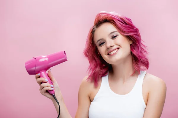 Mujer joven con pelo colorido sosteniendo secador de pelo aislado en rosa — Stock Photo