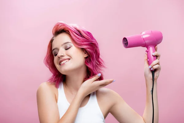 Mujer joven con el pelo colorido usando secador de pelo aislado en rosa — Stock Photo