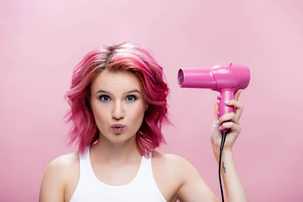 Mujer joven con pelo colorido sosteniendo secador de pelo y mueca aislado en rosa - foto de stock