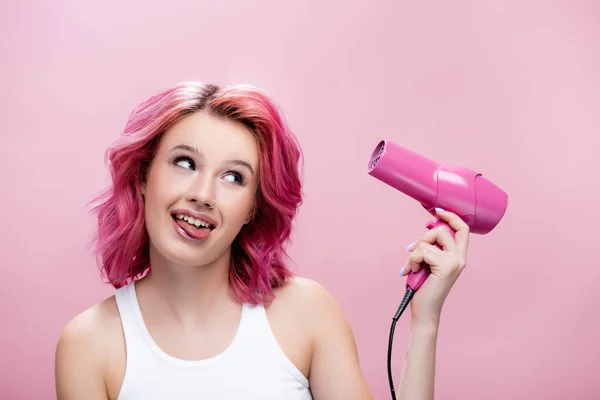 Jovem com cabelo colorido segurando secador de cabelo e sorrindo isolado em rosa — Fotografia de Stock