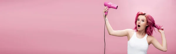 Scioccato giovane donna con capelli colorati utilizzando asciugacapelli isolato su rosa, colpo panoramico — Foto stock