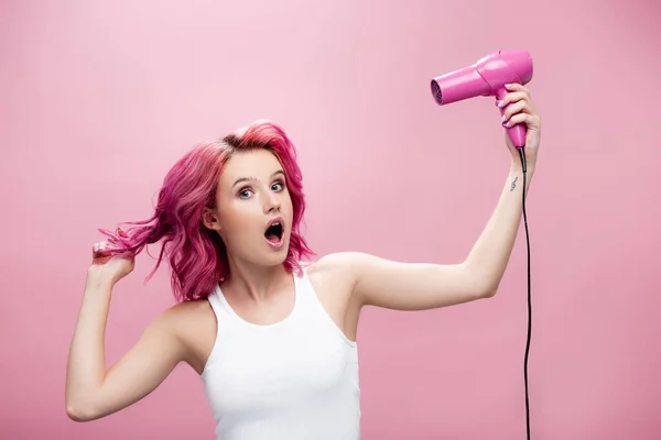 Scioccato giovane donna con capelli colorati utilizzando asciugacapelli isolato su rosa — Foto stock