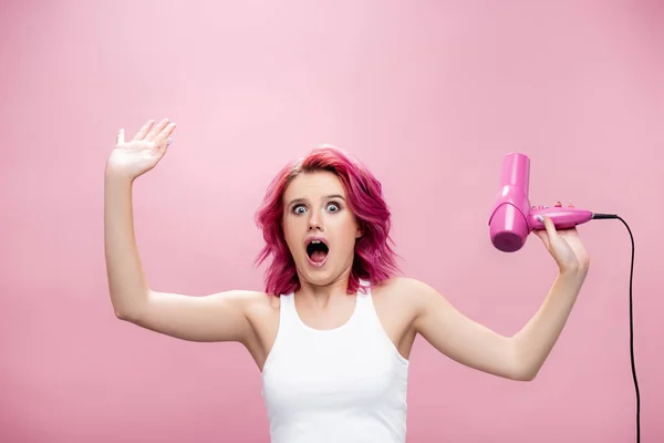 Scared young woman with colorful hair holding hairdryer isolated on pink — Stock Photo