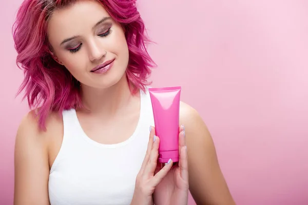 Jovem com cabelo colorido segurando tubo de creme cosmético isolado em rosa — Fotografia de Stock