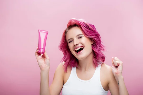 Молода жінка з барвистим волоссям тримає трубку косметичного крему ізольовано на рожевому — стокове фото