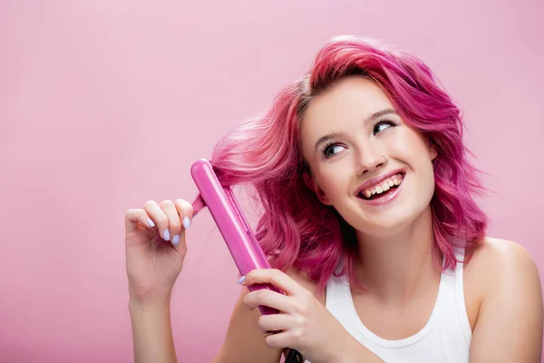 Young woman with colorful hair using straightener isolated on pink — Stock Photo