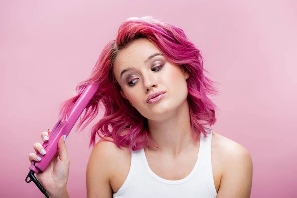 Jeune femme aux cheveux colorés utilisant redresseur isolé sur rose — Photo de stock