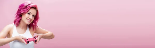 KYIV, UCRANIA - 29 de julio de 2020: mujer joven con el pelo colorido sosteniendo joystick aislado en rosa, tiro panorámico - foto de stock