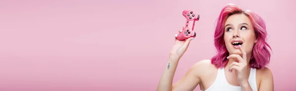 KYIV, UKRAINE - JULY 29, 2020: dreamy young woman with colorful hair holding joystick isolated on pink, panoramic shot — Stock Photo