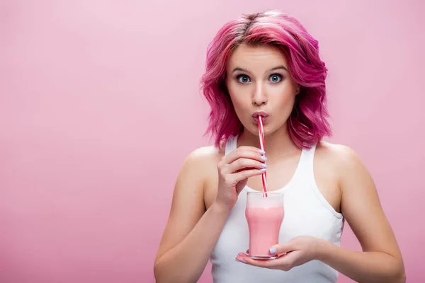 Überraschte junge Frau mit buntem Haar trinkt Erdbeer-Milchshake aus Stroh isoliert auf rosa — Stockfoto