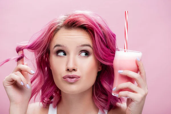Jovem sonhadora com cabelo colorido segurando milkshake de morango em vidro com palha de bebida isolada em rosa — Fotografia de Stock