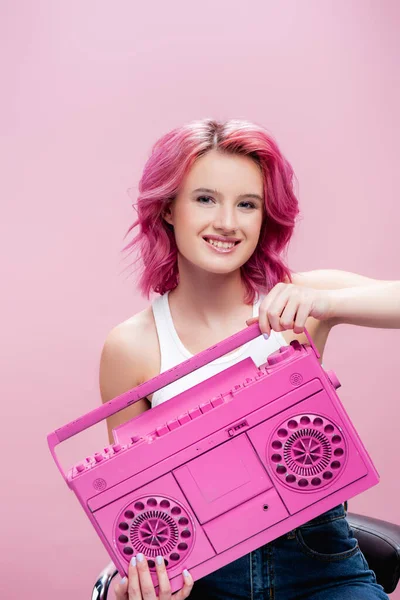 Mujer joven con pelo colorido sosteniendo grabadora de cinta pintada aislada en rosa - foto de stock