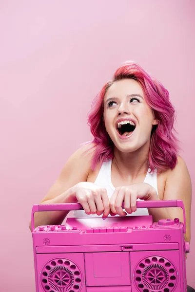 Aufgeregte junge Frau mit buntem Haar hält bemaltes Tonbandgerät isoliert auf rosa — Stockfoto