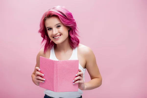 Giovane donna con i capelli colorati tenendo aperto libro isolato su rosa — Foto stock