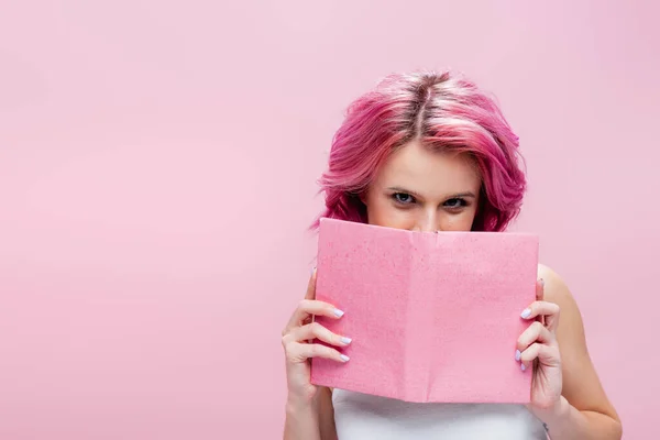 Junge Frau mit buntem Haar, Buch vor dem Gesicht isoliert auf rosa — Stockfoto