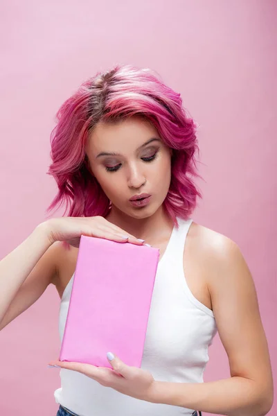 Jeune femme avec des cheveux colorés tenant livre isolé sur rose — Photo de stock