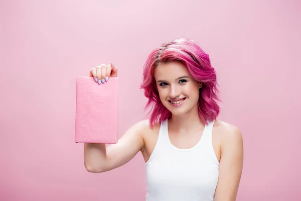 Mujer joven con pelo colorido presentar libro aislado en rosa - foto de stock