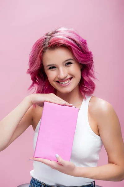 Young woman with colorful hair presenting book isolated on pink — Stock Photo