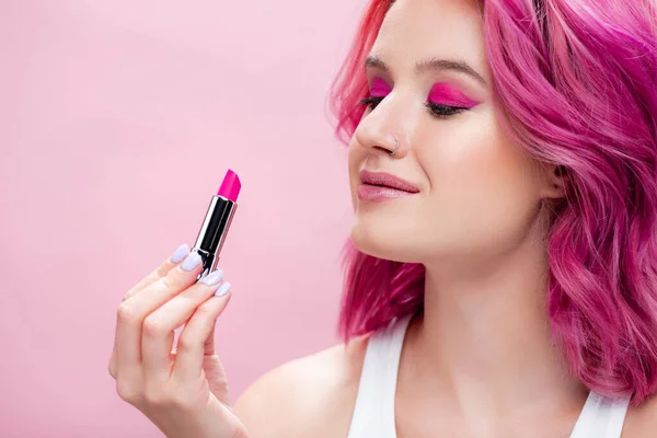 Young woman with colorful hair holding lipstick isolated on pink — Stock Photo