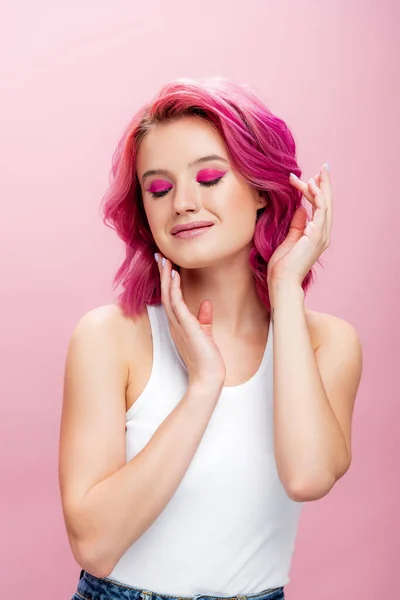 Mujer joven con el pelo colorido y maquillaje posando con las manos cerca de la cara y los ojos cerrados aislados en rosa - foto de stock