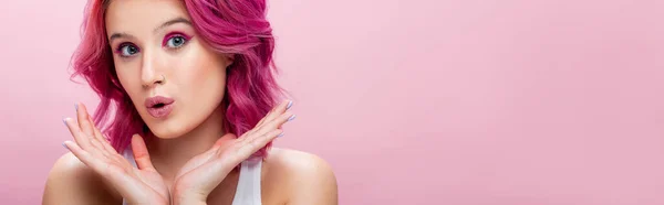 Sorpresa giovane donna con i capelli colorati e trucco posa con le mani vicino al viso isolato su rosa, colpo panoramico — Foto stock