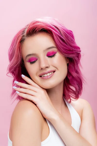 Mujer joven con el pelo colorido y maquillaje posando con la mano cerca de la cara aislada en rosa - foto de stock