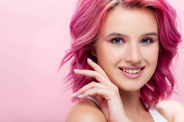 Giovane donna con capelli colorati e trucco in posa con mano vicino al viso isolato su rosa — Foto stock