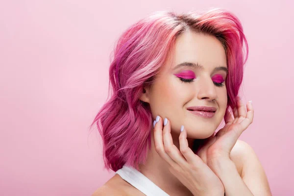 Mujer joven con el pelo colorido y maquillaje posando con las manos cerca de la cara aislada en rosa - foto de stock